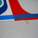 The fin with the tape shows just where to remove covering.  Use a sharp knife and careful not to score the wood.